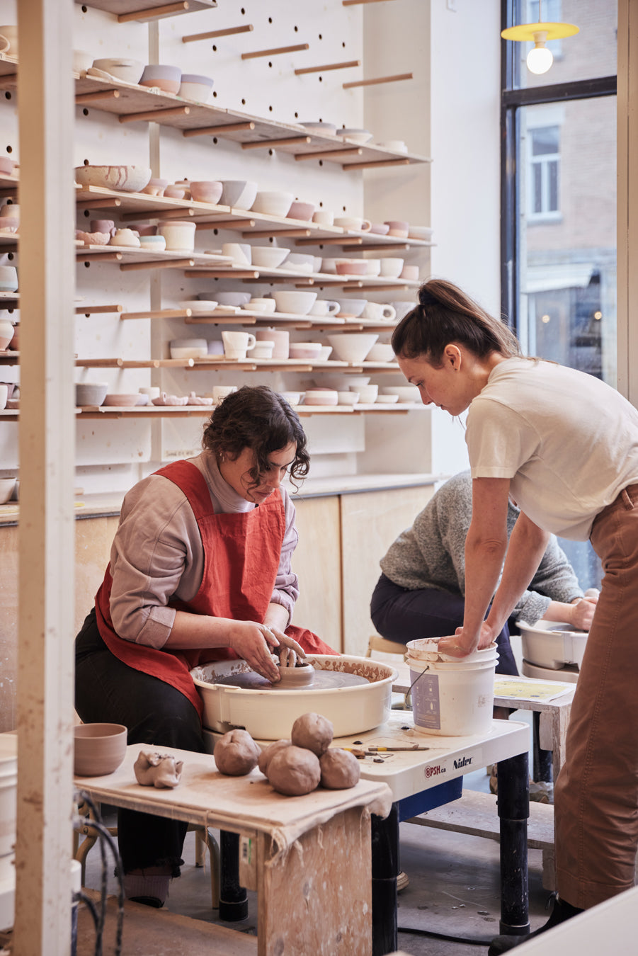 Professeure qui aide une étudiante à faire de la poterie sur le tour dans un atelier de poterie