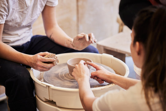 Professeure de poterie qui aide un étudiant à réaliser un bol en argile sur le tour de potier.