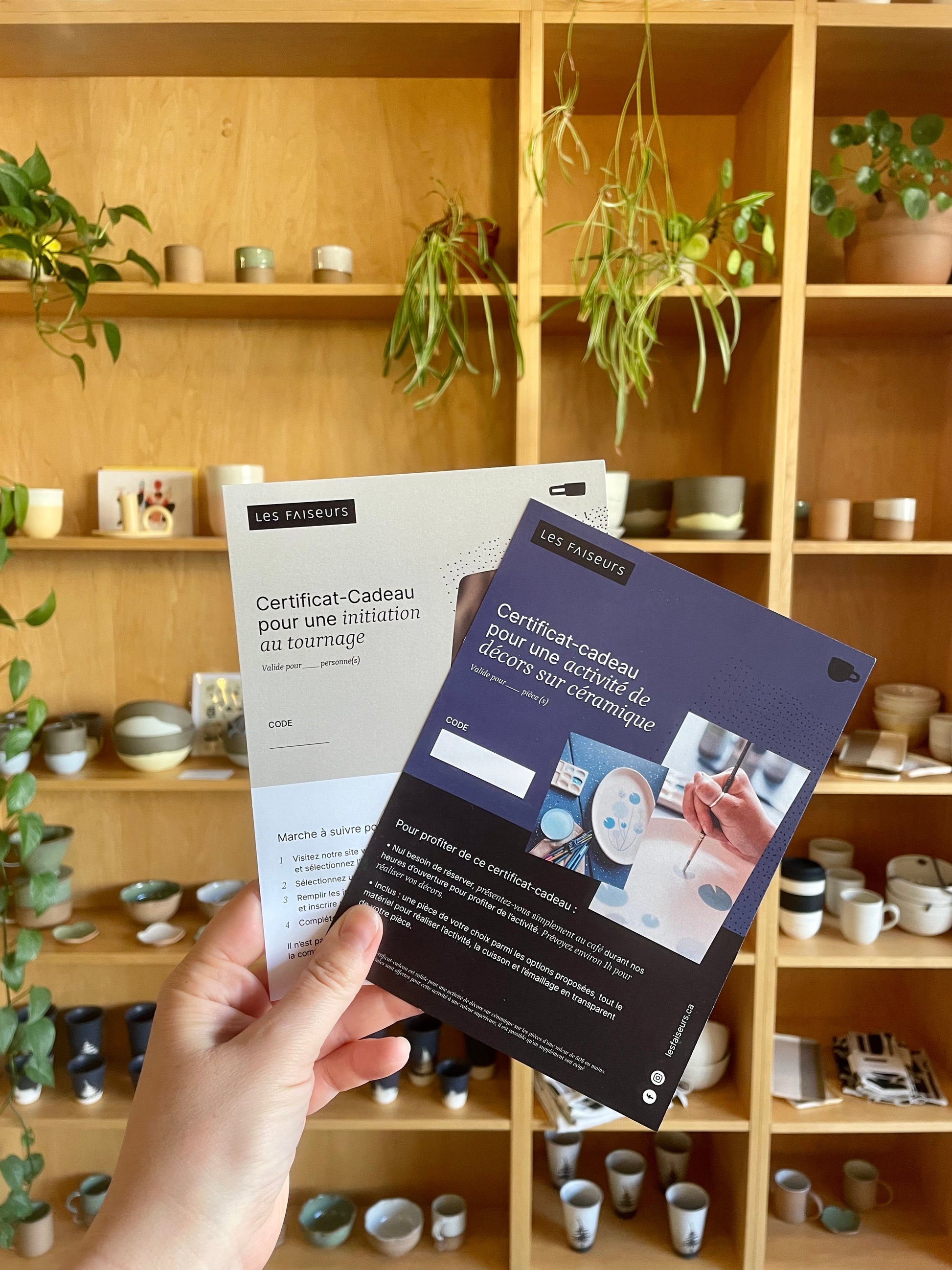 Main tenant des certificats-cadeaux devant une bibliothèque remplie de pièces de poterie.