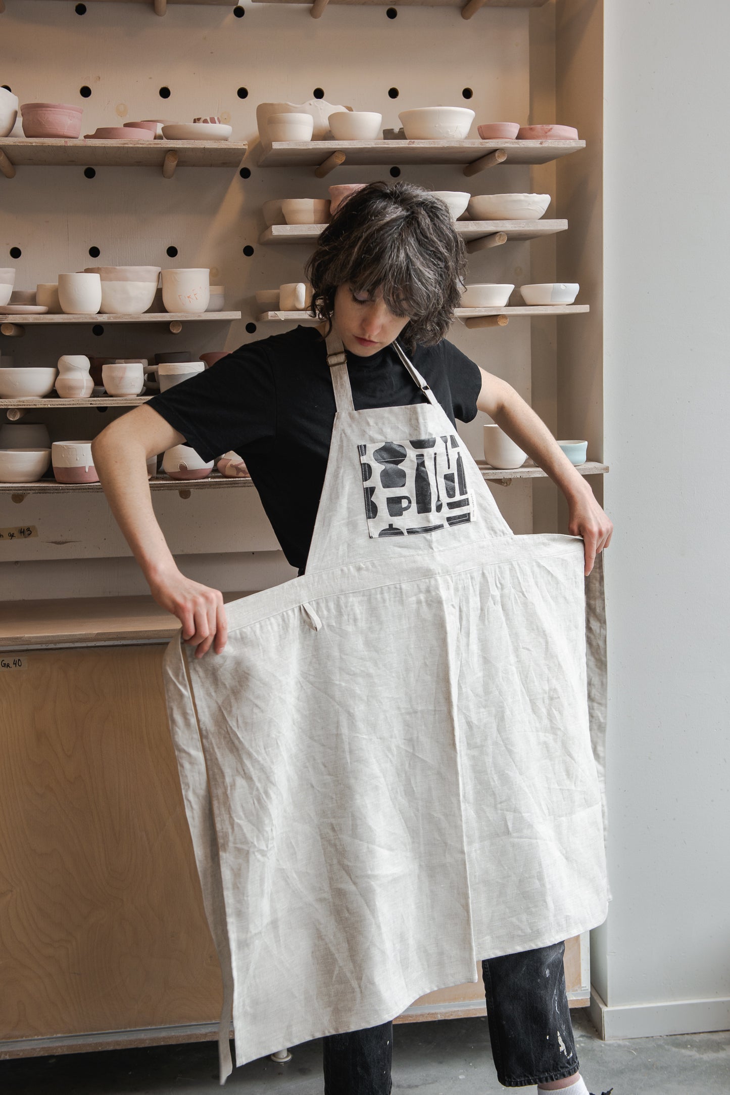 Femme qui met un tablier de poterie beige avec illustrations noires dessus