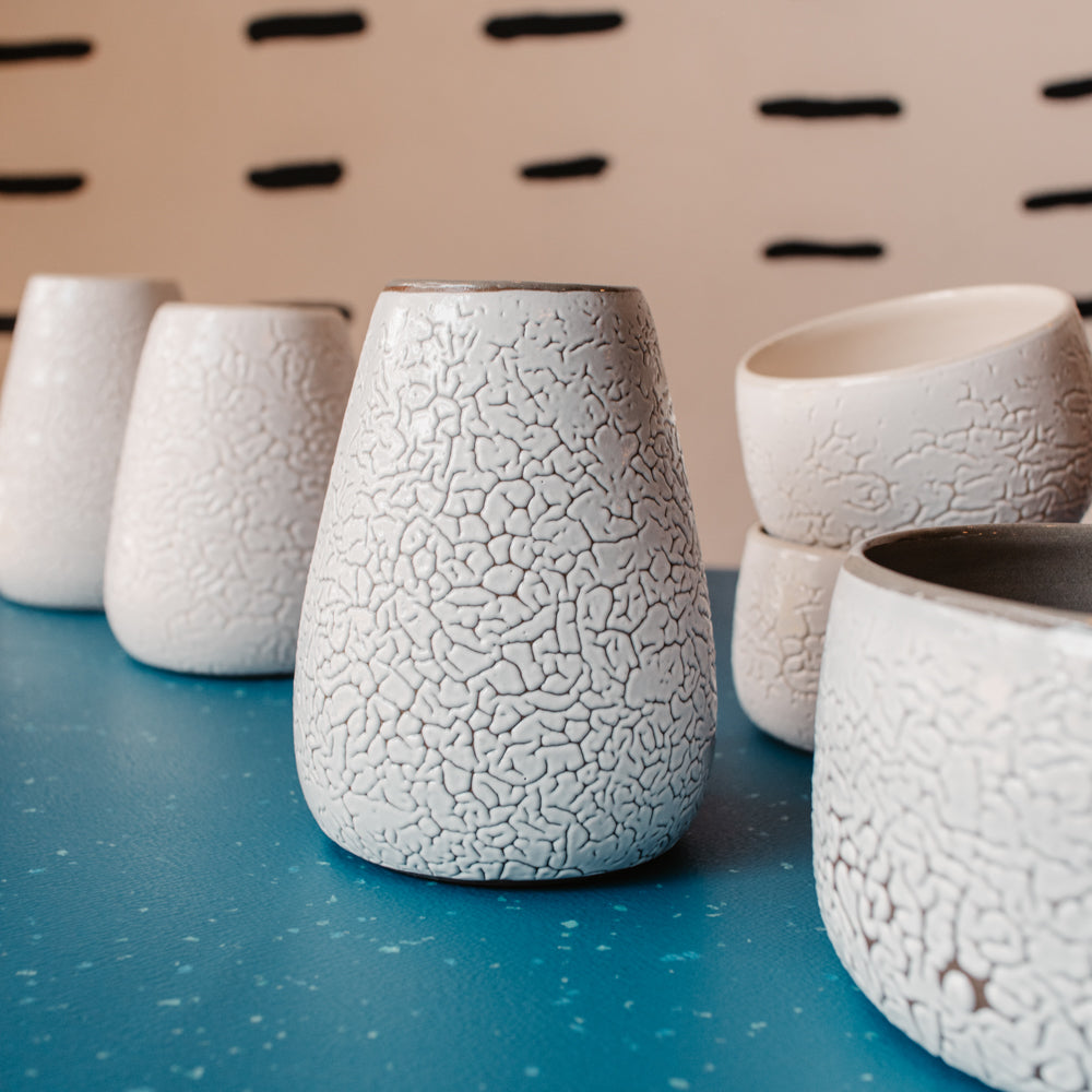 Des vases en céramique sont posés sur une table bleue. Une glaçure blanche qui se craquelle a été apposée sur les pièces.