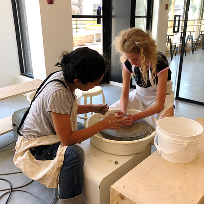 Professeure qui aide un enfant à réaliser une pièce de poterie sur un tour.