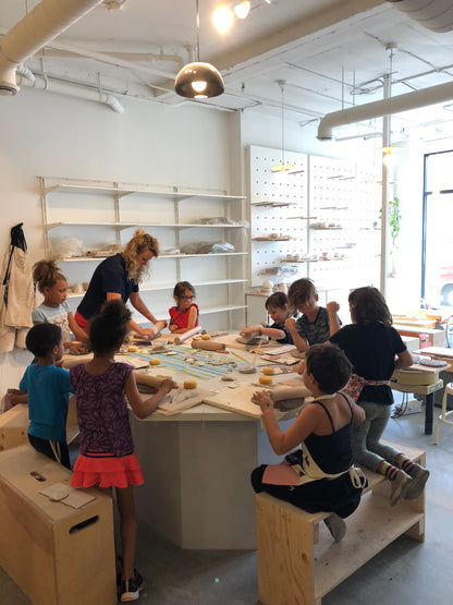 Groupe de 8 enfants autour d'une table qui font une activité de céramique avec une professeure