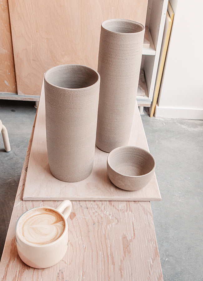 2 très hautes pièces de poterie sur une planche avec un petit bol et un café.