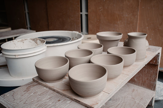 6 bols en poterie sur une planche à côté d'un tour de potier.
